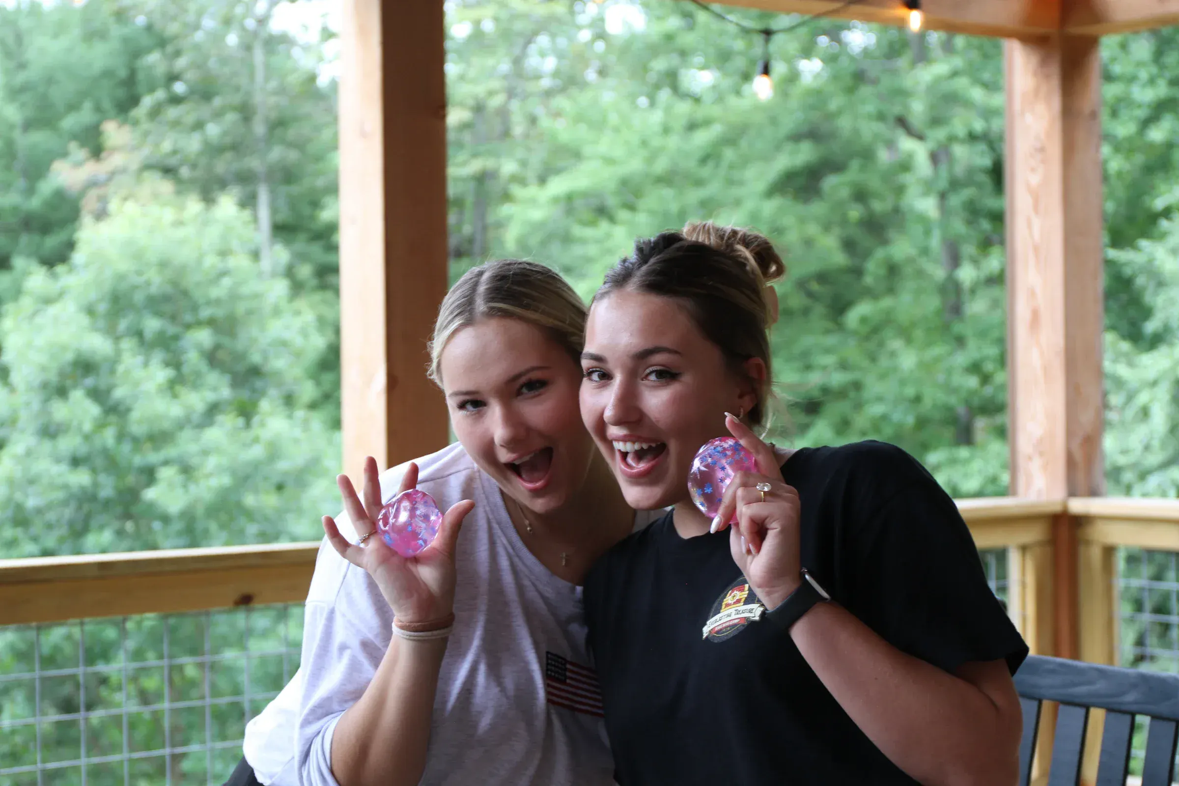 Two camp friends grin as they hold up glowing prizes on the porch.